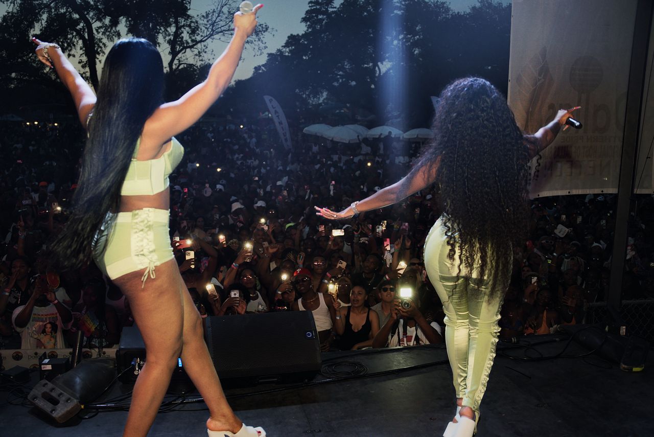 City Girls on stage at Dallas Southern Pride 2022, arms raised to a crowd holding up their phones